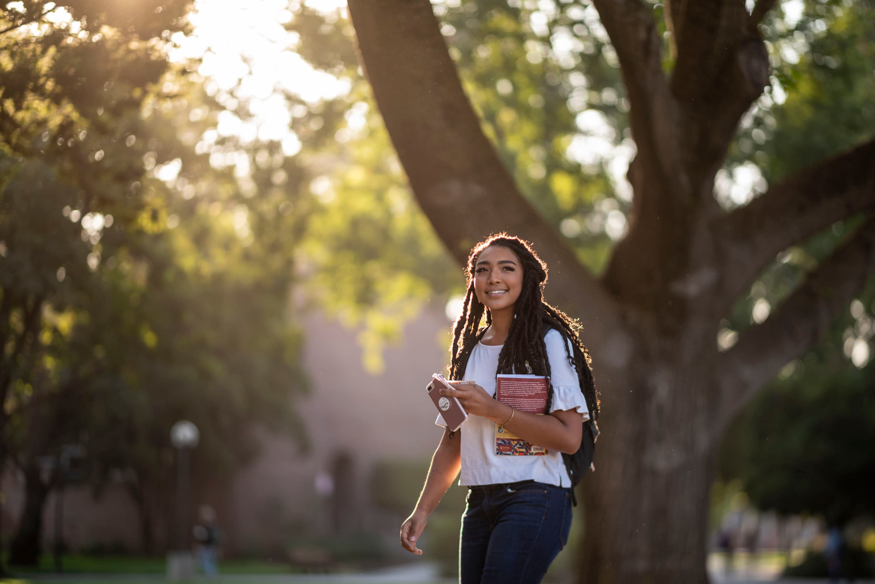 opportunities banner- female student holding a book, standing by a tree