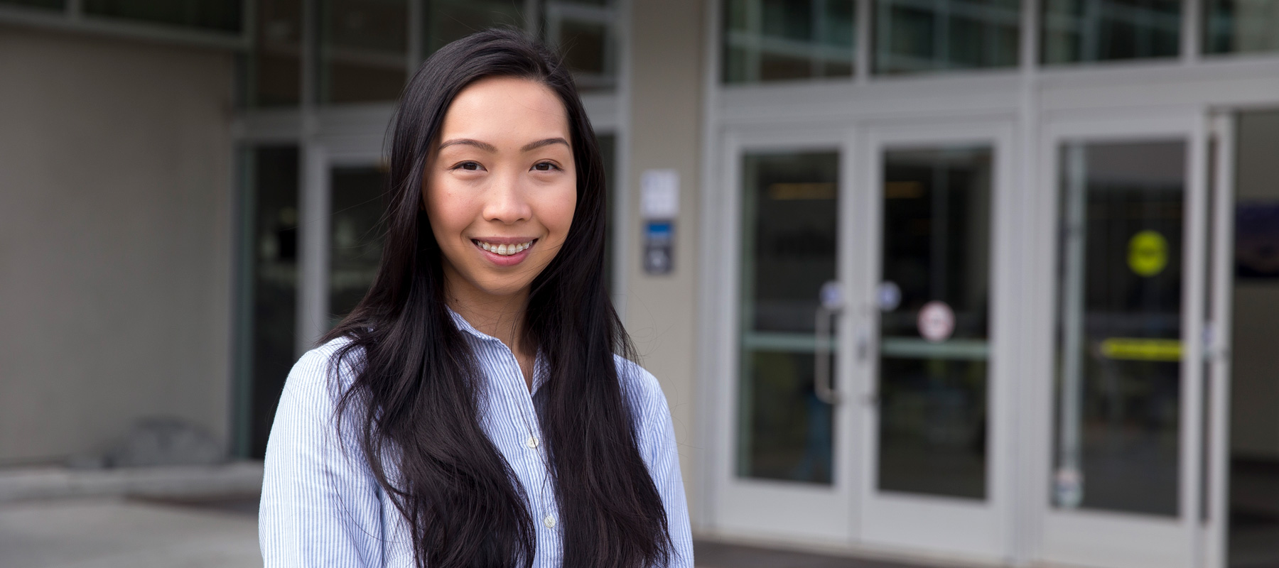 Iana Lim wearing a blue & white blouse smiling in front of a building