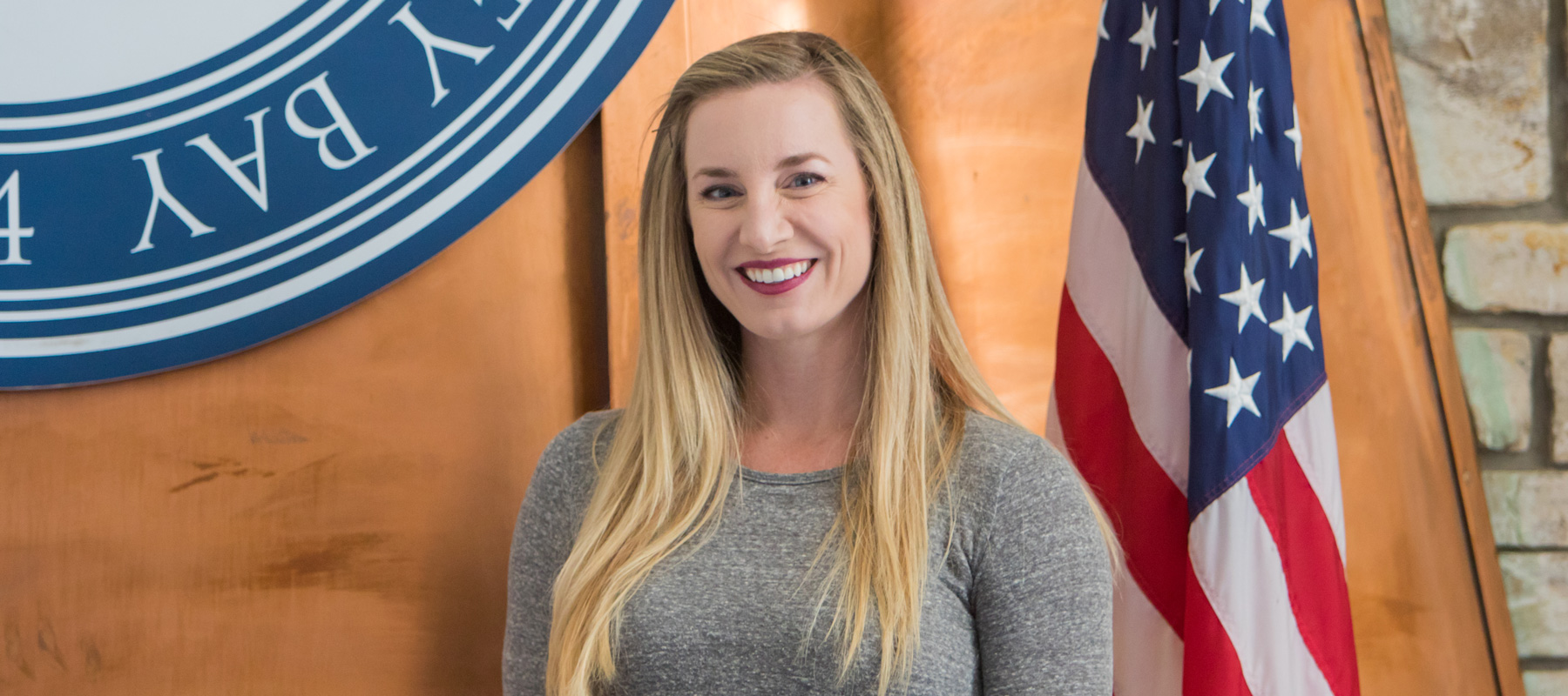 Lauren Kent wearing a gray shirt smiling next to an american flag