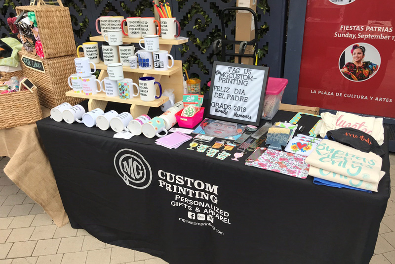 A table is set up with MG Custom Printing products.