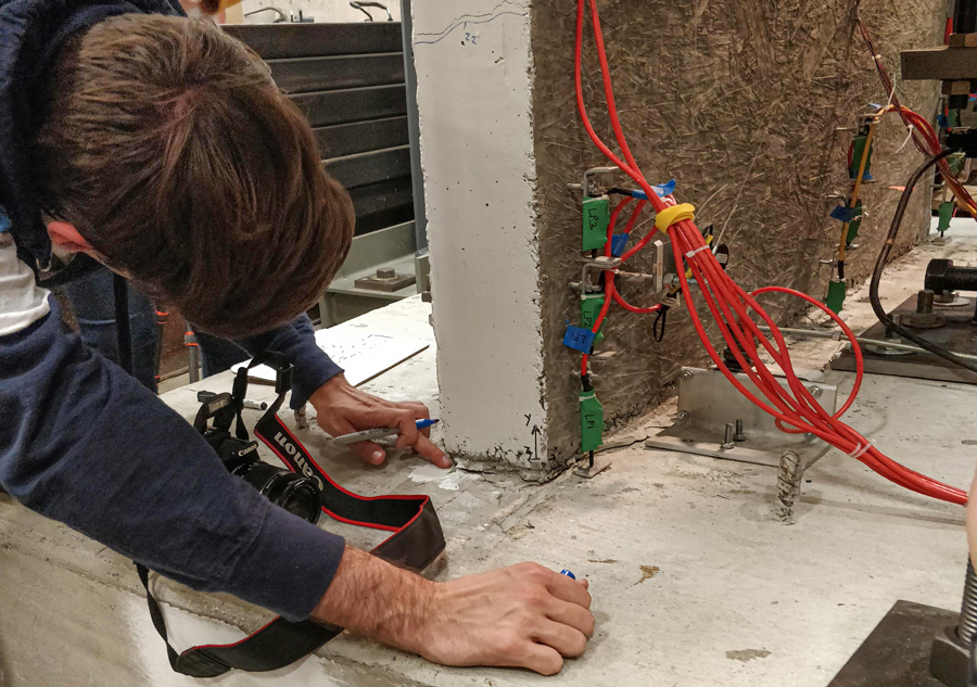 Architectural engineering student, Ryan Schwartz, documents cracks at the wall-foundation interface during a large-scale test of a lightly-reinforced concrete wall in 2019.