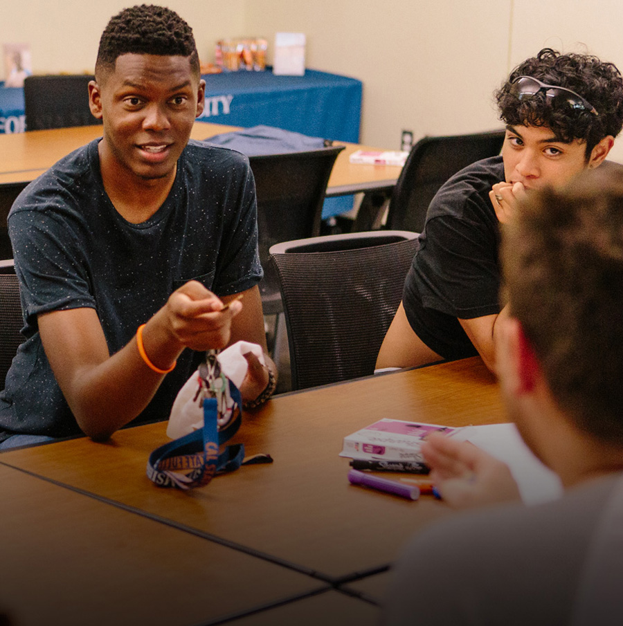Two male students talking across a table with campus staff