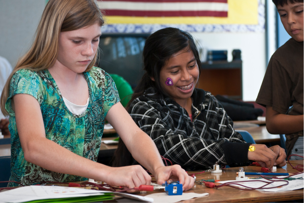young students gatherd around a table with a robot on it.