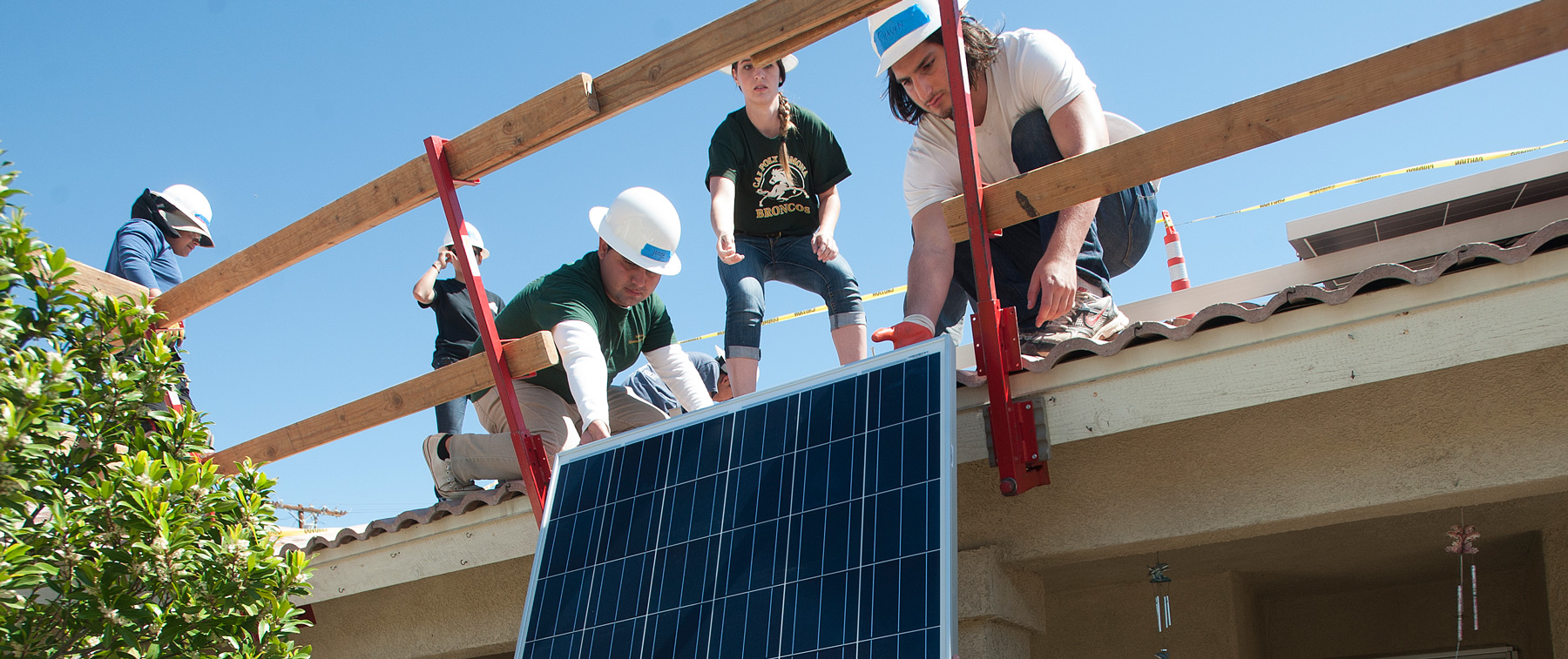 Three student builders putting solor pannel on roof of building
