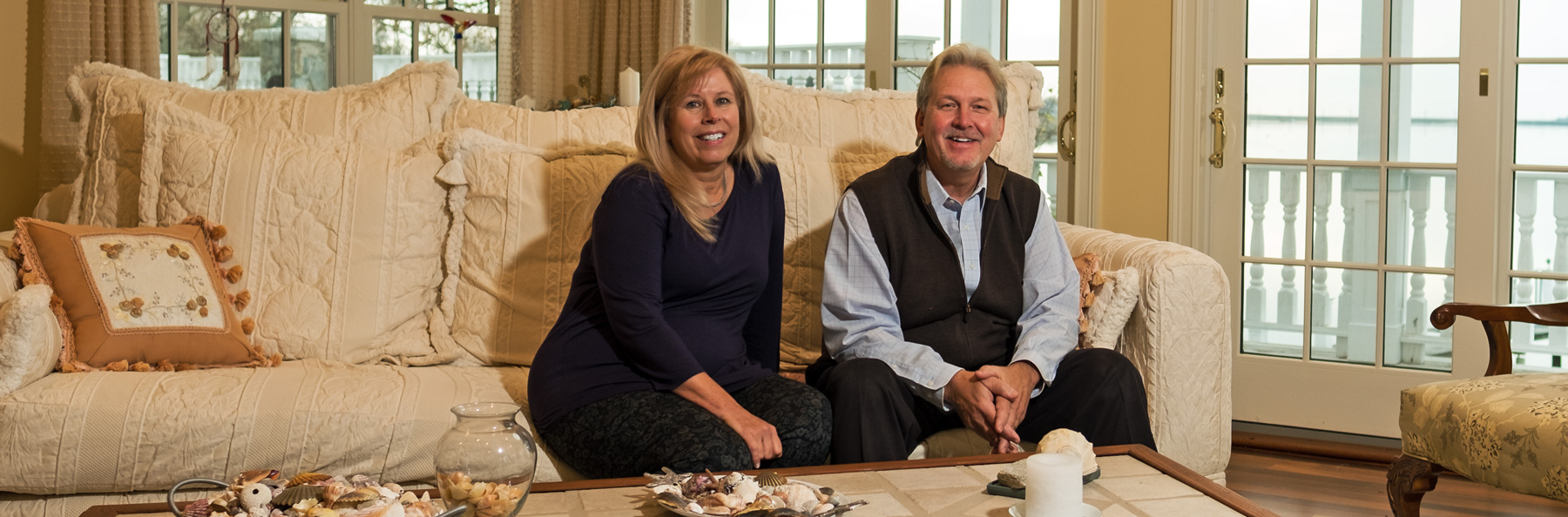 Ron and Mitzi Barhorst smiling sitting on a large light colored couch
