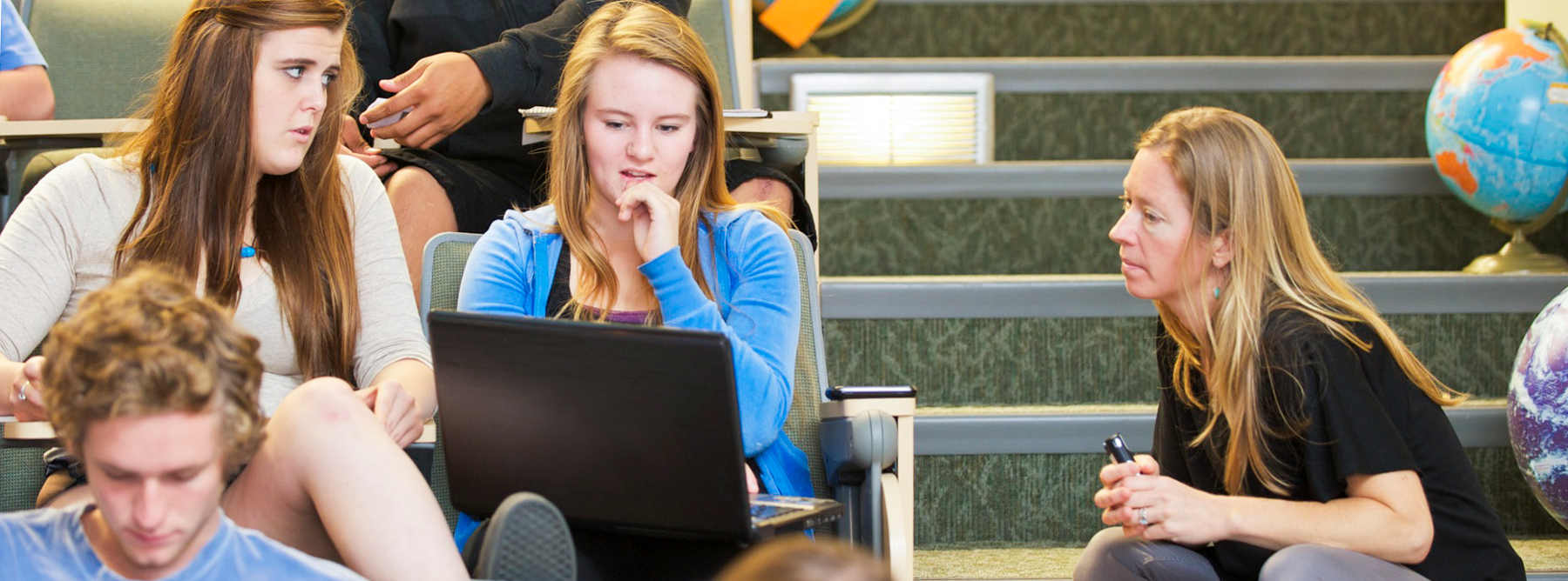 students and instructor looking at laptop in a lecture hall